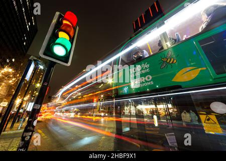 Ein Elektrobus, der behauptet, keine Emissionen zu setzen, wartet an der Ampel, Manchester, England, Großbritannien. Lange Belichtung mit leichten Spuren durch den Verkehr Stockfoto