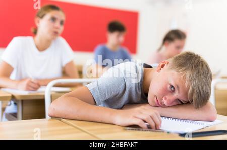 Gelangweilter Teenager, der während des Unterrichts am Schreibtisch im Klassenzimmer schläft Stockfoto