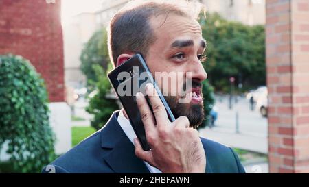 Porträt eines Geschäftsmannes, der am Telefon telefoniert und dem entfernten Kollegen die Marketingstrategie erklärt, während er vor den Büromitreisenden steht. Kollegen, die sich nicht einig sind. Outdoor-Konzept Stockfoto