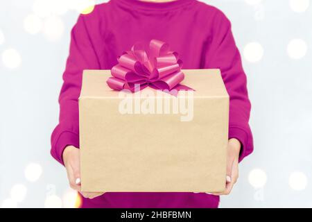 Geschenke in den Händen der Frau. Express-Lieferung. Eine junge Frau in einem violetten Sweatshirt hält eine Pappschachtel mit Schleife. Stockfoto