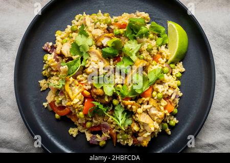 Hühnercrüy mit grünen Erbsen, rotem Pfeffer, Koriander, Limette und Basmati-Reis, serviert auf einem dunklen Teller. Stockfoto