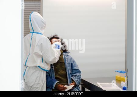 Schwarze Frau, die vor dem Einsteigen in den Flughafen Faro, Portugal, von einer Krankenschwester in schützendem PSA-Anzug sitzt, um einen Schnelltest (SARS-CoV-2 Rapid Antigen Test) zu erhalten Stockfoto