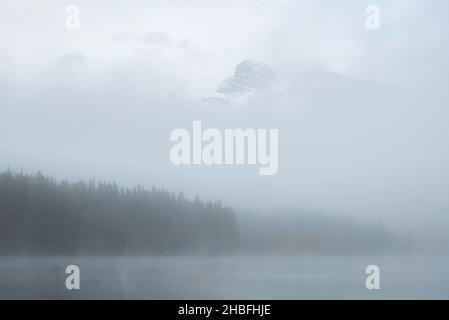 Ein geheimnisvoller Morgen am Two Jack Lake in Banff, während Nebel den Großteil der Szene umhüllt und nur ein Gipfel über dem Nebel aufragt. Stockfoto