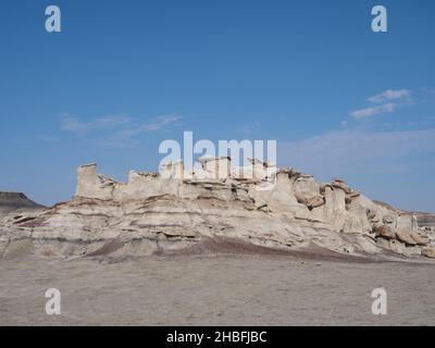 Ein Ausbiss aus erodiertem beigefarbenem Felsen mit Sockeln und Kappen in Bisti Badlands oder De-Na-Zin Wilderness in New Mexico mit spärlichen Wolken darüber. Stockfoto