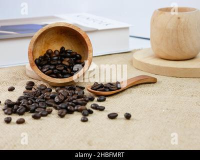 Hölzerne Tasse Kaffee mit Kaffeebohnen und Buch mit verschwommenem Hintergrund. Morgendliche Aktivitäten Stockfoto