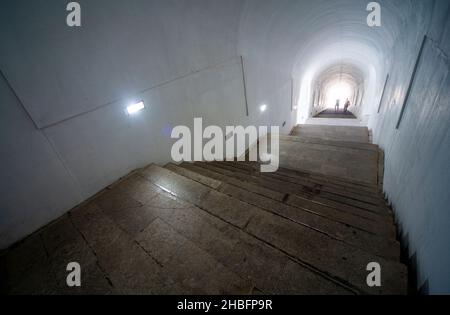 Lovcen Nationalpark. Schwach beleuchtete steile, weiße Steintreppen, die durch einen langen schmalen Tunnel im Berg hinauf zum Mausoleum von Petar II Petrovic führen. Stockfoto