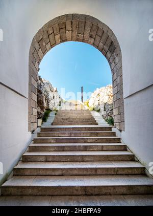 Lovcen Nationalpark. Schwach beleuchtete steile, weiße Steintreppen, die durch einen langen schmalen Tunnel im Berg hinauf zum Mausoleum von Petar II Petrovic führen. Stockfoto