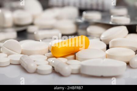Gelbe Medikamentenkapsel zwischen weißen Tabletten Stockfoto