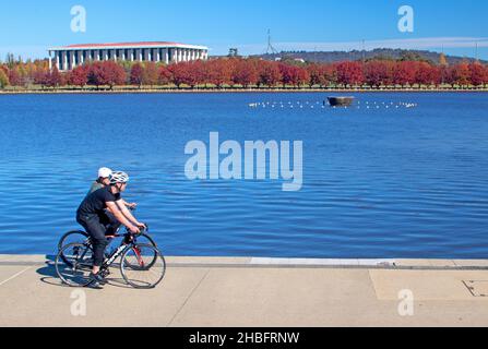 Radfahren am Ufer des Lake Burley Griffin, mit der Nationalbibliothek auf der anderen Seite des Sees Stockfoto