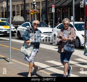 Zwei aktive, stylische Frauen, die auf einem Zebra in der Innenstadt von Victoria BC spazieren. Ältere Frauen überqueren die Straße. Stockfoto