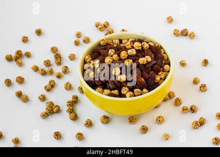 Doppelt geröstete gelbe Kichererbsen und schwarze Rosinen in gelber Schale auf weiß, oben Stockfoto