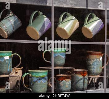 In der Töpferwerkstatt stehen verschieden farbige Tonkappen auf dem Regal. Bunte Becher im Regal im Geschenkeladen des Einzelhändlers. Stockfoto