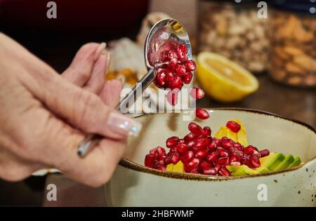 Der Koch fügt Granatapfelkerne zu einem Obstsalat zu Hause in der Küche hinzu Stockfoto