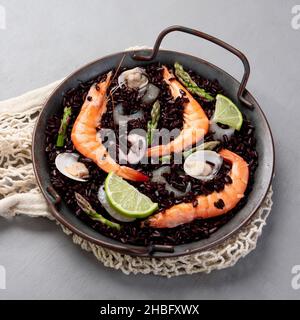 Schwarze Paella mit Meeresfrüchten auf grauem Hintergrund. Mediterrane Ernährung. Traditionelles Food-Konzept. Stockfoto