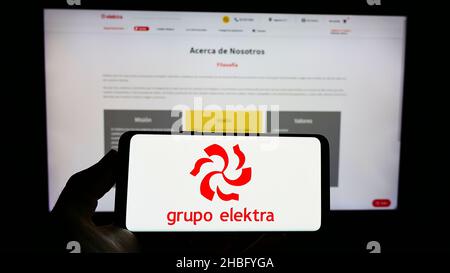 Person, die das Smartphone mit dem Logo des mexikanischen Einzelhandelsunternehmens Grupo Elektra auf dem Bildschirm vor der Website hält. Konzentrieren Sie sich auf die Telefonanzeige. Stockfoto