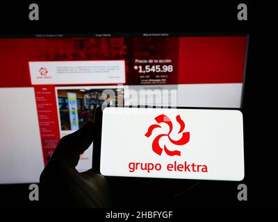 Person, die ein Mobiltelefon mit dem Logo des mexikanischen Einzelhandelsunternehmens Grupo Elektra auf dem Bildschirm vor der Unternehmenswebseite hält. Konzentrieren Sie sich auf die Telefonanzeige. Stockfoto