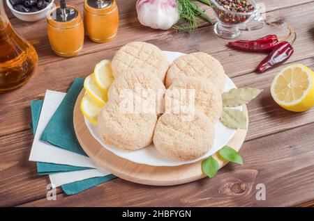 Frische Koteletts, Halbfertigprodukte für Burger aus Geflügelfleisch auf einem weißen Teller auf dunklem Holzboden. Stockfoto