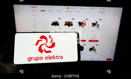 Person mit Mobiltelefon und Logo des mexikanischen Einzelhandelsunternehmens Grupo Elektra auf dem Bildschirm vor der Business-Webseite. Konzentrieren Sie sich auf die Telefonanzeige. Stockfoto