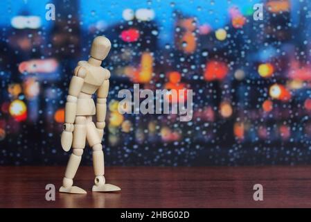 Hölzerne menschliche Figur traurig und Enttäuschung auf Holztisch vor regnerischen Tag Fenster Hintergrund Stockfoto