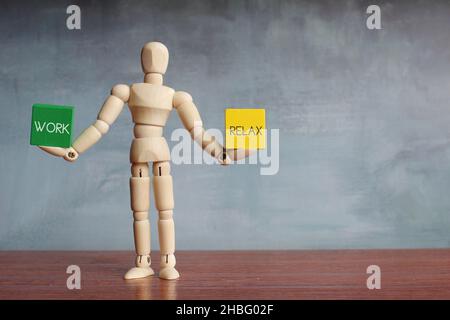 Hölzerne menschliche Figur balanciert Holzwürfel mit Text ARBEITEN und ENTSPANNEN. Stockfoto