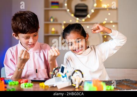 Kinder wurden begeistert und feiern nach dem erfolgreichen Abschluss der Herstellung diy Roboter zu Hause - Konzept der Kindheit Wissenschaft Experiment, Geschwister verbinden Stockfoto