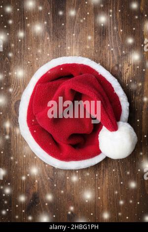 Weihnachtsmann Hut auf einem hölzernen Hintergrund mit fliegenden Schneeflocken. Weihnachten, Neujahr Stockfoto