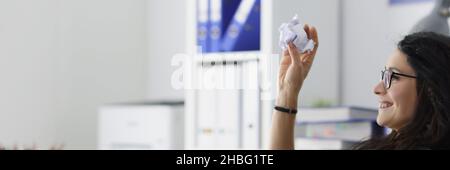 Lächelnde Geschäftsfrau, die am Tisch sitzt und zerknittertes Papier wirft Stockfoto
