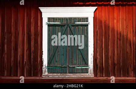 Ein abgenutztes Fenster, das mit grünen Holzfenstern bedeckt ist Stockfoto