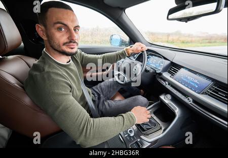 Porträt eines hübschen jungen Mannes, der beim Fahren eines modernen Autos auf die Kamera schaut. Stockfoto