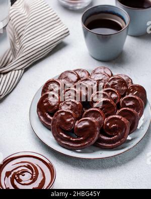 Schokoladen-palmierteig in Keramikplatte auf hellgrauem Betontisch mit schwarzem Kaffee und geschmolzener Schokolade in Schale, Draufsicht Stockfoto