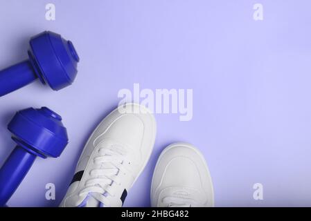 Weiße Sport-Sneakers Schuhe und blaue Kurzhanteln auf dem blauen Hintergrund. Stockfoto
