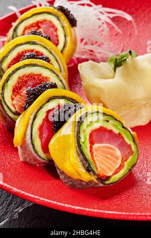 Sushi-Rollen mit Lachs, Thunfisch, Tobiko, Avocado in mamenori, gekrönt mit Mango, schwarzem Kaviar auf rotem Teller Stockfoto