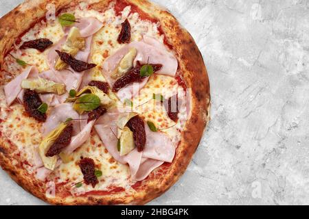 Pizza mit Kalbfleisch, Schinken, Käse und getrockneten Tomaten auf einem grauen Tisch. Stockfoto