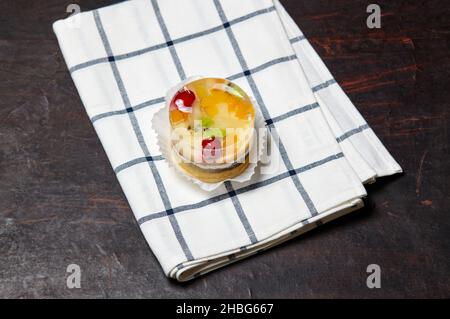 Kuchen mit Gelee, Kiwi, Kirschen und Mango auf dem Tisch. Leckeres Mini-Dessert auf einem hölzernen Hintergrund, Nahaufnahme. Stockfoto