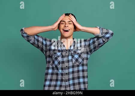 Halblanges Porträt eines jungen schockierten Mannes, Studenten, der mit aufhebenden Händen auf grünem Studiohintergrund isoliert steht. Stockfoto