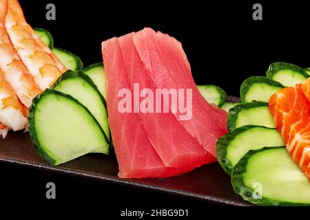 Nahaufnahme von rohem Thunfisch-Sashimi auf einer Platte mit Lachs, Garnelen und Gurke Stockfoto