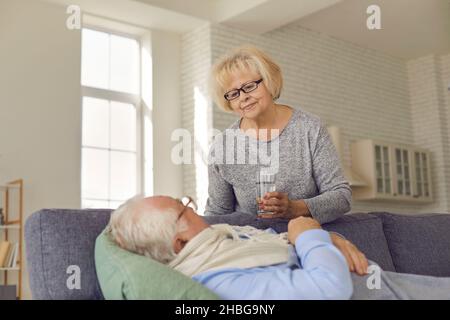 Beziehung eines Geliebten. Fürsorgliche ältere Frau gibt ihrem grippekranken Mann ein Glas Wasser. Stockfoto