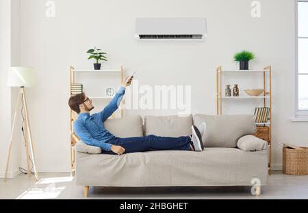 Mann mit Fernbedienung von der Klimaanlage macht bequeme Temperatur für sich. Stockfoto