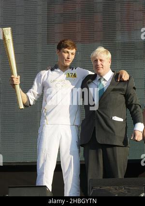 Tyler Rix und der Bürgermeister Boris Johnson mit der olympischen Fackel beim London 2012 Olympic Fackel Relay Concert von Coca-Cola im Hyde Park in London. Stockfoto