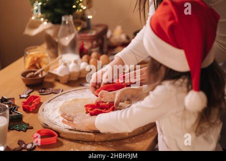 Lebkuchen zu Hause machen. Kleines Mädchen mit ihrer Mutter, die Kekse aus Lebkuchenteig schneidet. Weihnachts- und Neujahrstraditionen Konzept. Weihnachtsbäckerei Stockfoto