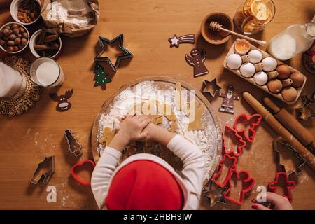 Lebkuchen zu Hause machen. Kleines Mädchen, das Kekse aus Lebkuchenteig schneidet. Weihnachts- und Neujahrstraditionen Konzept. Weihnachtsbäckerei. Glücklich Stockfoto