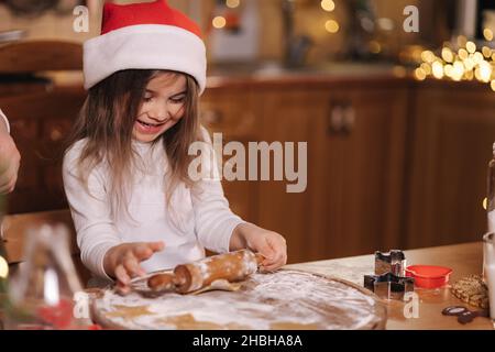 Lebkuchen zu Hause machen. Kleines Mädchen, das Kekse aus Lebkuchenteig schneidet. Weihnachts- und Neujahrstraditionen Konzept. Weihnachtsbäckerei. Glücklich Stockfoto