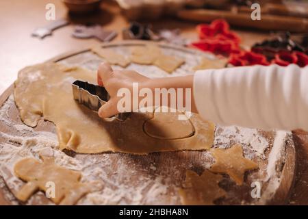 Lebkuchen zu Hause machen. Kleines Mädchen, das Kekse aus Lebkuchenteig schneidet. Weihnachts- und Neujahrstraditionen Konzept. Weihnachtsbäckerei. Glücklich Stockfoto