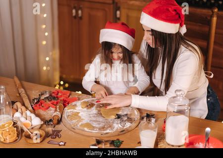 Lebkuchen zu Hause machen. Kleines Mädchen, das Kekse aus Lebkuchenteig schneidet. Weihnachts- und Neujahrstraditionen Konzept. Weihnachtsbäckerei. Glücklich Stockfoto