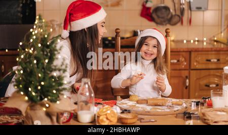 Prozess der Mutter und Tochter Backen zu Hause. Roher Teig zum Kochen Weihnachtskekse Lebkuchen auf Holztisch. Kerzenlicht am Abend. Fir Stockfoto