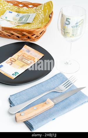 Konzeptuelle Studioaufnahme des Esstisches mit Euro-Banknoten auf dem Teller statt des Essens. Konzept für steigende Lebensmittelpreise, Inflation, Wirtschaftskrise Stockfoto