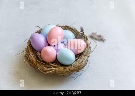 Frohe Ostern Konzept. Vorbereitung auf den Urlaub. Bunt verzierte ostereier im Nest mit Feder auf betonsteingrauem Hintergrund. Einfacher Minimalismus flach Lay Draufsicht Kopierraum Stockfoto