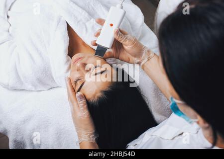 Draufsicht auf eine Frau, die im Spa-Salon Ultraschallkavitation-Gesichtspeeling erhält. Ultraschallwäscher für die Kosmetologie. Entfernung von Akne. Stockfoto