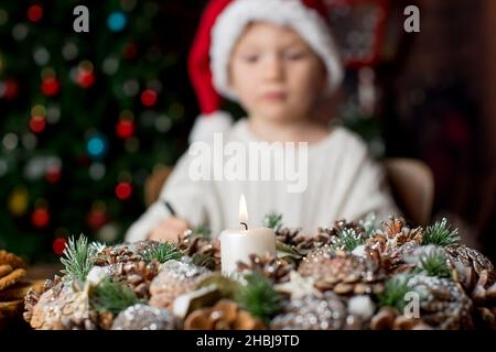 Adventskranz mit brennender Kerze in der Mitte, Kinderbrief im Hintergrund, weihnachtsbaum dahinter Stockfoto