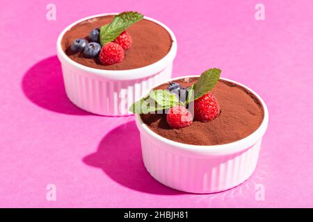 Perfekter hausgemachter Tiramisu-Kuchen mit frischer Minze. Tiramisu Teil in weißer Platte auf rosa Hintergrund harte Schatten. Stockfoto